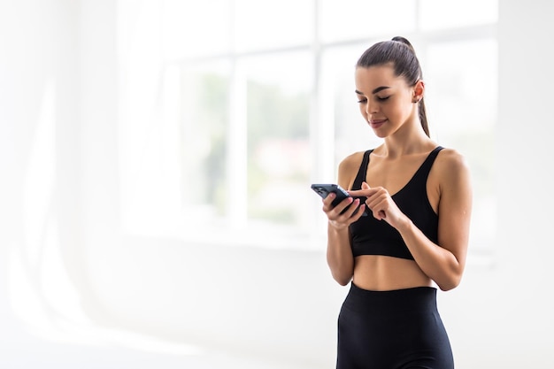 Attractive healthy young woman with a fitness mat using mobile phone at the gym