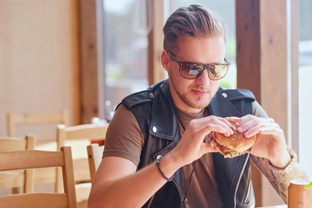 Attraente hipster vestito con una giacca di pelle che mangia un hamburger vegano.