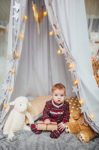 Attractive infant girl  playing with her toys on gray wall. She love her white ram and teddy bear.