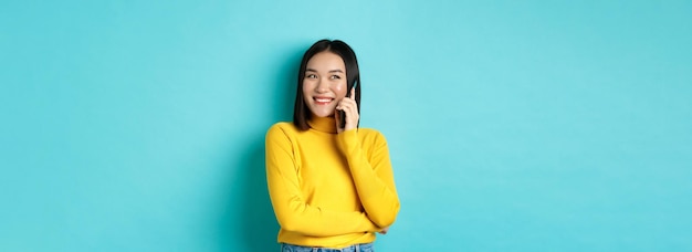 黄色いセーターを着た魅力的な韓国人女性が会話をし、笑顔で携帯電話で話している