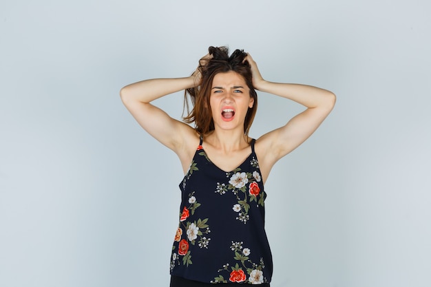 Attractive lady in blouse holding hands on head and looking scared , front view.