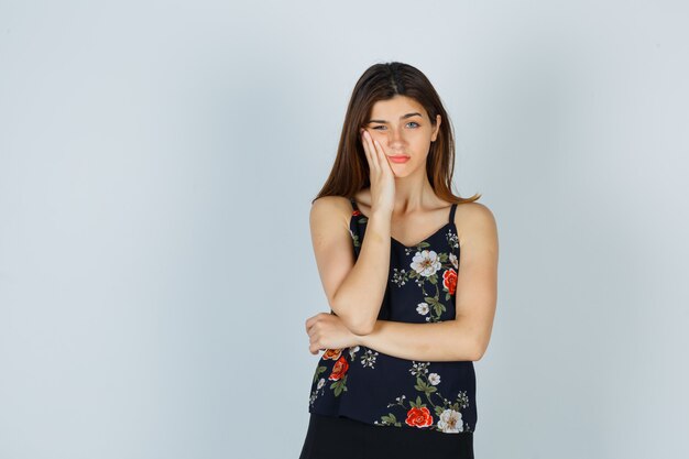 Attractive lady in blouse keeping hand on cheek and looking displeased , front view.