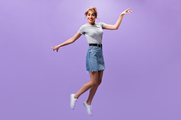 Attractive lady in denim outfit jumping.n purple background. Beautiful young woman in shirt and stylish skirt posing.n isolated backdrop.