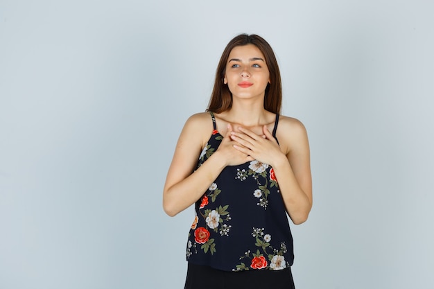 Attractive lady holding hands on chest in blouse and looking pleased , front view.