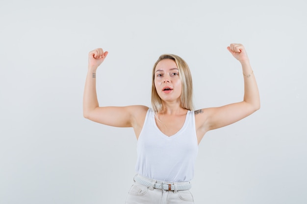 무료 사진 흰 블라우스에 그녀의 근육을 보여주는 그녀의 팔을 올리고 자신감을 보이는 매력적인 아가씨