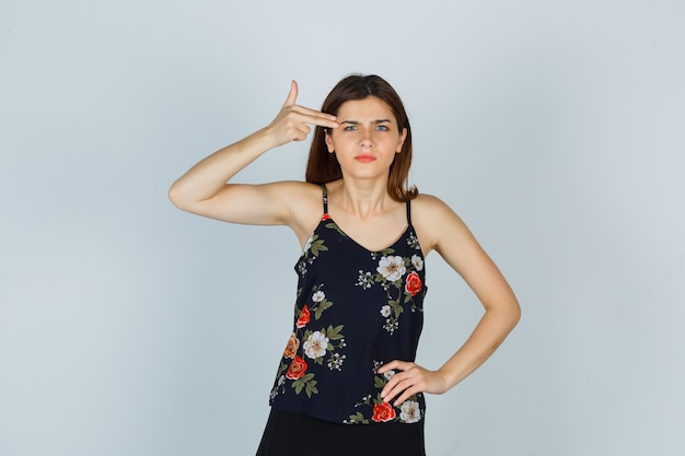 Attractive lady showing suicide gesture in blouse and looking irritated , front view.