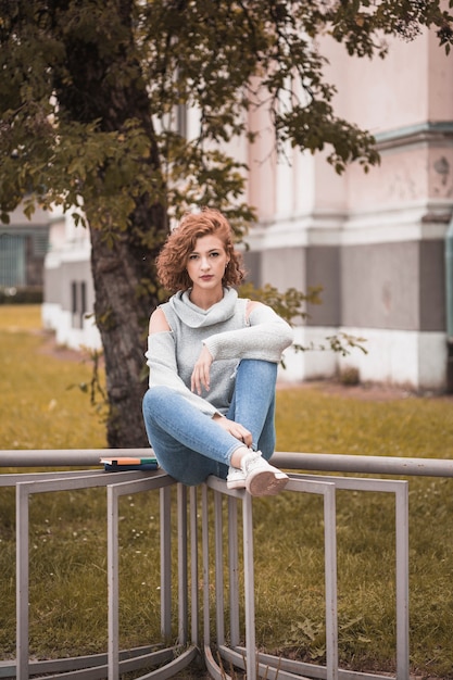 Free photo attractive lady in street wear sitting on rail