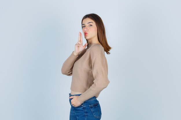 Attractive lady in sweater, jeans making hand gun sign, pouting lips and looking cool