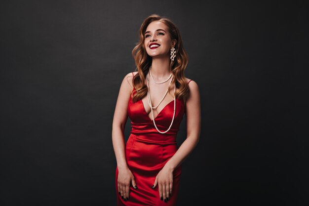 Attractive lady wearing red dress and jewelry with pearls laughing on black background