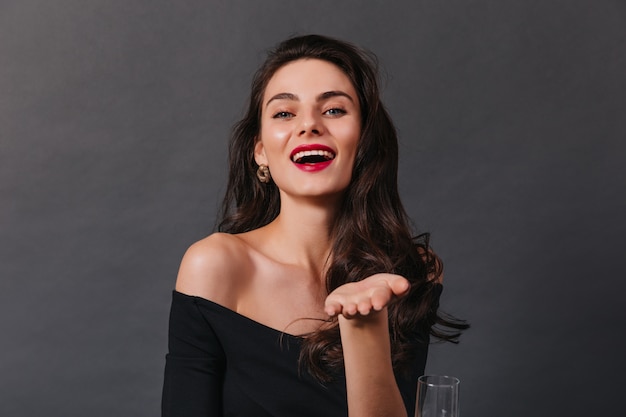 Attractive lady with curly hair in dark top laughs and looks into camera on black background.