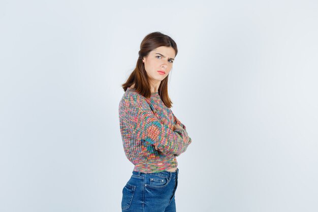 Attractive lady with hands crossed in sweater, jeans and looking displeased .