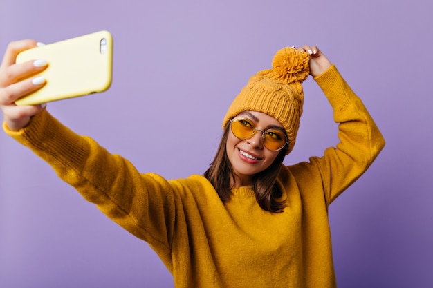 Attractive lady with soft features makes selfie on her yellow smartphone. Portrait of slavic student in good mood