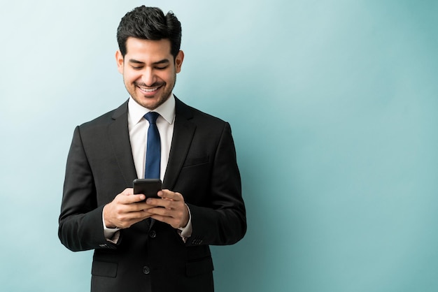 Привлекательный латинский бизнесмен обменивается текстовыми сообщениями через мобильный телефон на цветном фоне