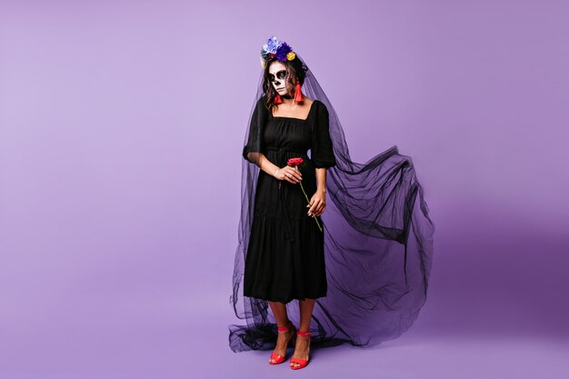 Attractive latin girl posing in long black veil in day of the dead. Charming vampire lady celebrating halloween alone.