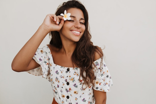 Attractive long-haired brunette woman with infinity sign on her wrist smiling on white wall