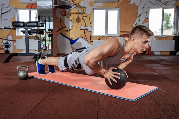 Attractive male athlete performing push-ups on medicine ball. Exercising at the gym