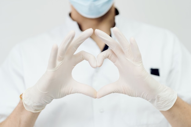 Привлекательный мужской доктор показывает знак сердца с руками, изолированными на белой стене