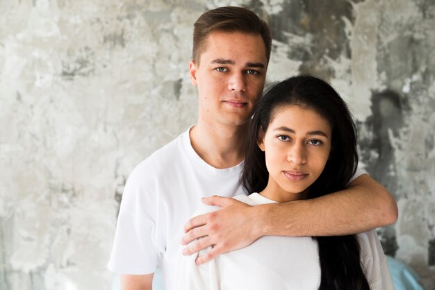Attractive male embracing ethnic girlfriend and looking at camera