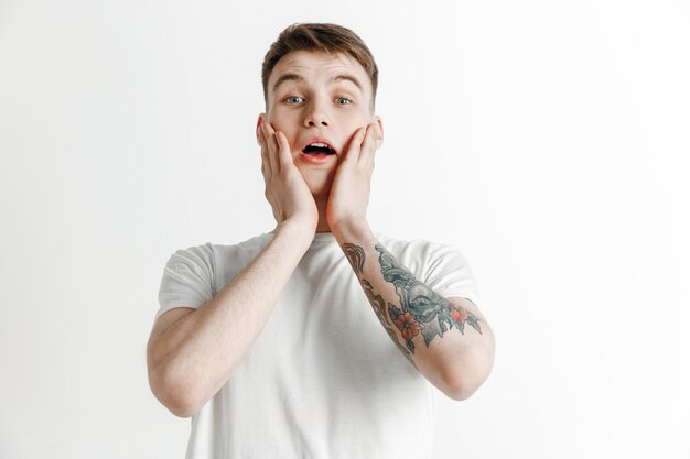 Attractive male half-length front portrait on gray studio backgroud. Young emotional surprised man standing with open mouth. Human emotions, facial expression concept