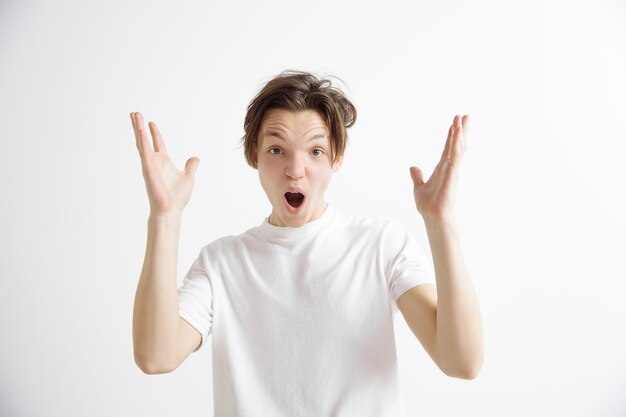 Attractive male half-length front portrait on gray studio backgroud. Young emotional surprised man standing with open mouth. Human emotions, facial expression concept