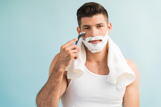 Attractive man grooming himself with napkin on shoulder while making eye contact against plain background