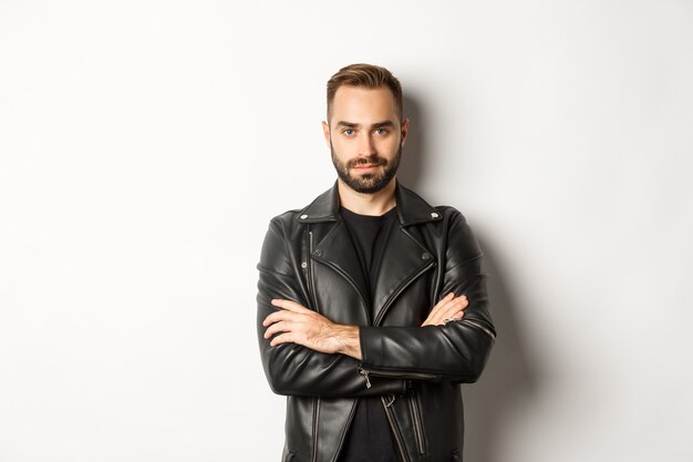 Attractive  man in leather jacket smiling, looking confident with hands crossed on chest