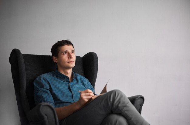 Attractive man in plaid blue shirt writing new ideas into notebook with pen