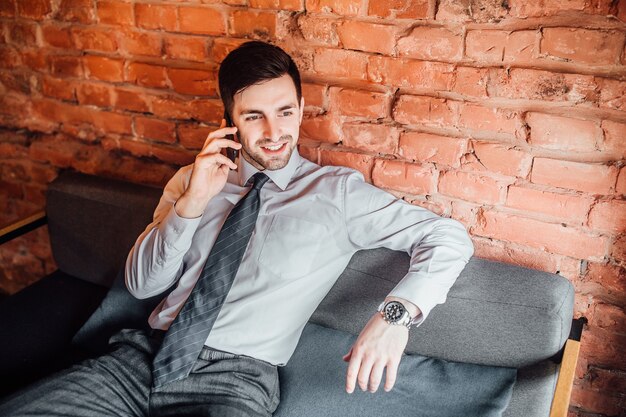 Attractive man in suit sits relaxed at the sofa and talks on the phone