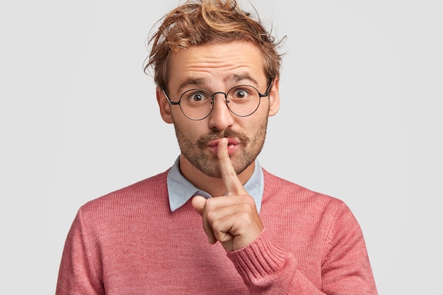 Free photo attractive man tells secret to close friend, hopes for loyalty and silence, makes hush gesture, wears casual outfit