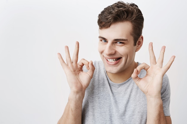 Attractive man with blue eyes, smiling with joy showing ok sign with both hands, glad after meeting with his girlfriend isolated . Human facial expressions and emotions