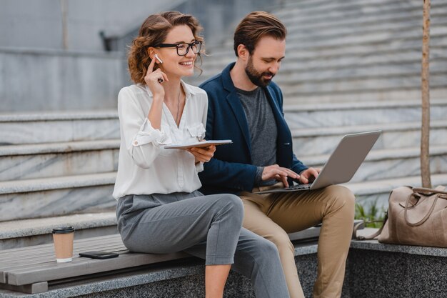 Attractive man and woman sitting on stairs in urban city center, working together on laptop,