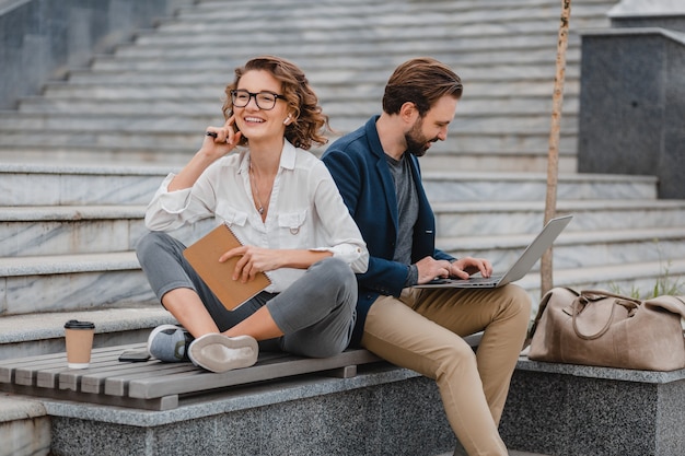 Attractive man and woman sitting on stairs in urban city center, working together on laptop