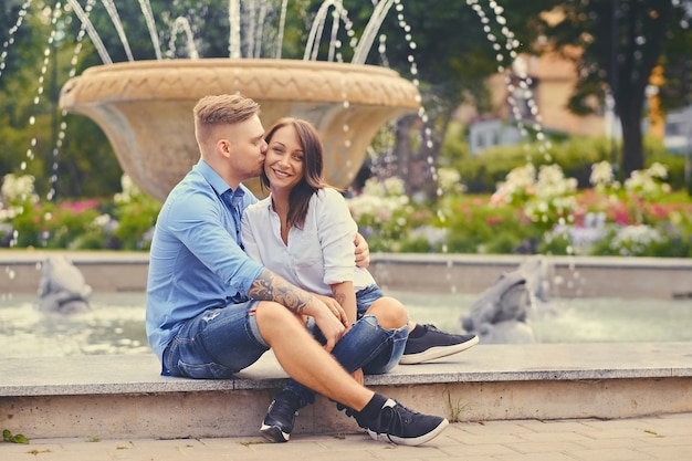 無料写真 デートの魅力的な現代のカップルは、街の噴水の上でポーズをとっています。
