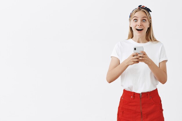 Attractive modern girl using mobile phone and looking surprised