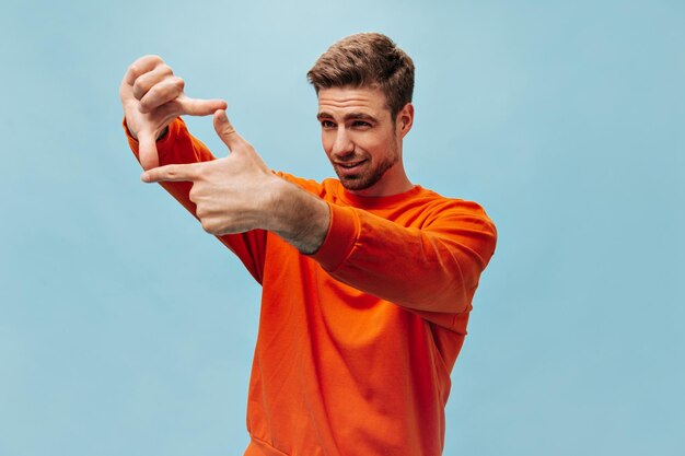 Attractive modern guy with stylish hairstyle and beard in cool sweatshirt posing and looking away on isolated blue background