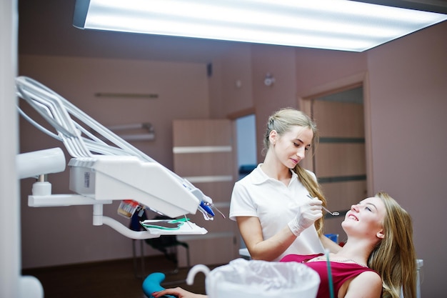 Paziente attraente in abito rosso viola sdraiato sulla poltrona del dentista mentre il dentista femminile si cura i denti con strumenti speciali