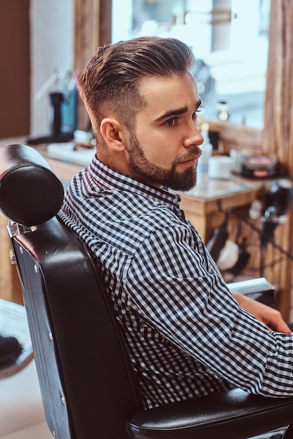 魅力的な物思いにふける男は、忙しい理髪店で散髪をする順番を待っています。