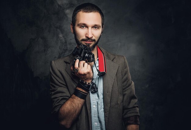 Attractive pensive man with photo camera is posing for photographer at dark photo studio.