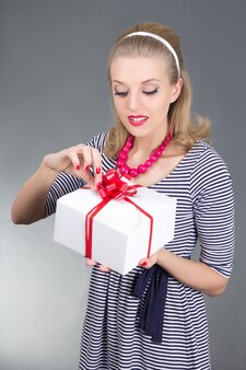 Привлекательная девушка кинозвезды в полосатом платье открытия подарка над серым