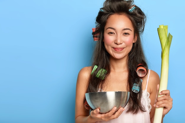 Free photo attractive positive asian lady holds green leek, steel bowl, going to chop vegetable