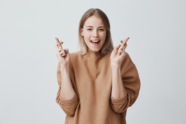 Il modello femminile positivo attraente con capelli biondi incrocia le dita come speranze