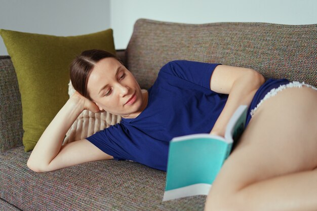 Attractive positive woman reading a book relaxing on the sofa