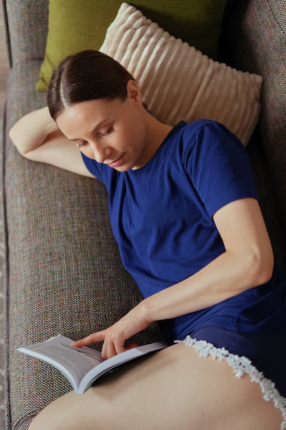 Attractive positive woman reading a book relaxing on the sofa