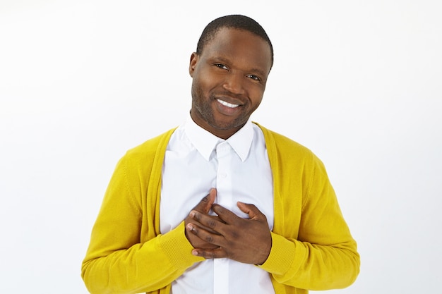 Attractive positive young Afro man looking at camera with open appreciative smile, keeping hands on his chest, demonstrating gratitude, feeling thankful for help. Human emotions, reaction and feelings