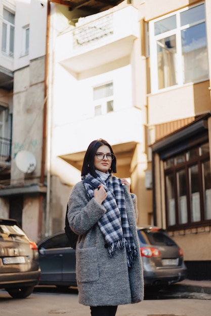 Бесплатное фото Привлекательная позитивная молодая девушка в очках в пальто на улице