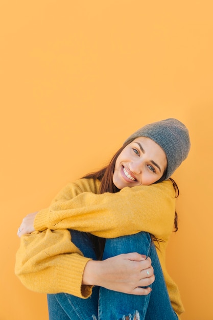 Free photo attractive pretty woman looking at camera sitting in front of yellow backdrop