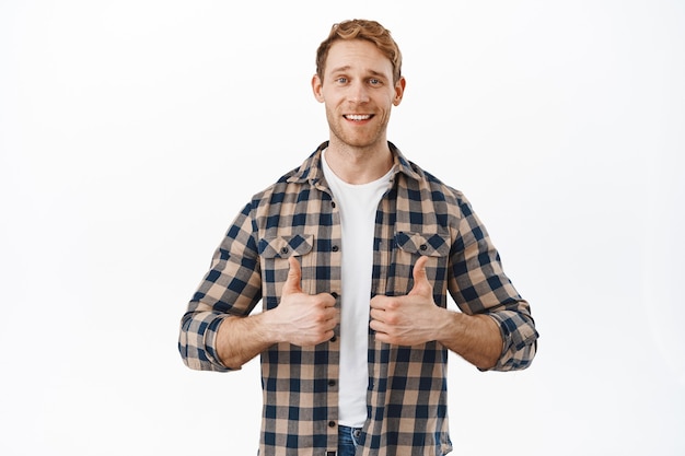 Attractive redhead adult man showing thumbs up and smiling happy, satisfied with quality, praise and agree, making compliment, well done great job gesture