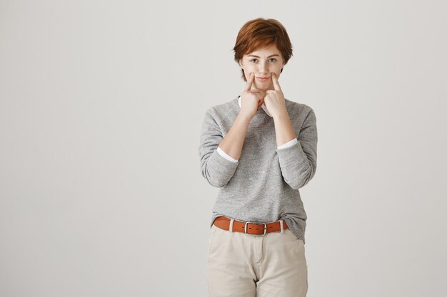 Attractive redhead girl with short haircut posing against the white wall