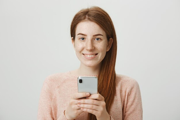 Привлекательная рыжая улыбающаяся девушка с помощью мобильного телефона, обмена сообщениями