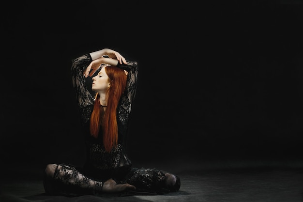 An attractive redheaded girl in black lingerie poses in the studio